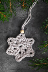 Wall Mural - White crochet snowflake close up and fir tree branches on a grey background. Handmade cotton Christmas decor.