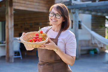 Wall Mural - Smiling woman in apron showing branch of ripe red yellow cherry tomatoes