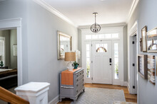 An open large and wide interior front door hallway foyer with transom, hanging light fixture, coastal colors and entry way table and wood floors