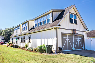 The rear back side of a long cottage style new construction cream white house with tan trim and a basketball hoop with a manicured lawn