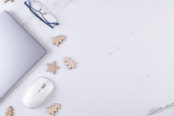 Modern office workspace with laptop, mouse and eye glasses with Christmas wooden decoration. Business concept flat lay on white marble background. Creativity and innovation concept, copy space