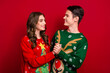 © deagreez - Photo of cheerful positive couple wife husband wear ugly pullovers look each other enjoy xmas event day isolated on red color background