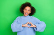 Leinwandbild Motiv Portrait of toothy beaming stylish girl with wavy coiffure wear blue oversize pullover showing heart isolated on green color background