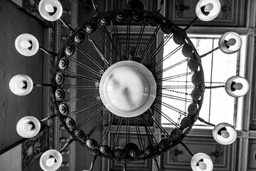 Canvas Print - Closeup shot of a chandelier in the church ceiling in grayscale with a window in the background