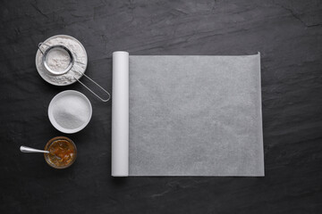 Roll of baking parchment paper and ingredients on black slate background, flat lay