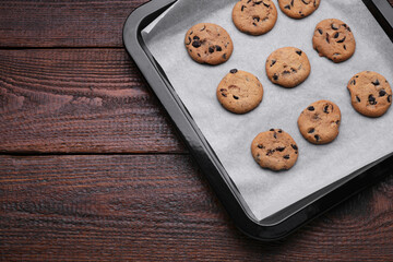 Baking pan with cookies and parchment paper on wooden table, top view. Space for text