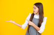 Surprised emotions of young teenager girl. Portrait of cute teenager child girl pointing hand showing adverts with copy space over yellow background.
