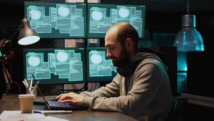 Stressed IT coder hacking security system on computer, using pc malware to steal big data from server. Working at night with multiple monitors to hack database, being irritated. Handheld shot.