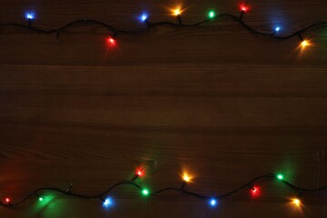 Wall Mural - Frame of colorful Christmas lights on wooden table, top view. Space for text