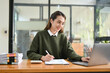 © bongkarn - Beautiful Asian businesswoman working at her desk, using laptop, managing her financial report.