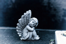 Vintage Dirty Statue Angel On Tomb Stone In Old Cemetery.  Small Winged Angelic Figurine On Dark Grave Yard