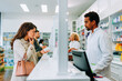 © bernardbodo - Woman purchasing cough medication in pharmacy.