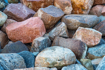 Wall Mural - Close-up of a pile of large granite stones with a fine texture. Background with a protective embankment of pebbles on the beach.