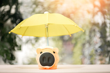 Wall Mural - The yellow umbrella for protect to sick piggy bank on sunlight in the public park, to prevent for asset and saving money for buy health insurance concept.