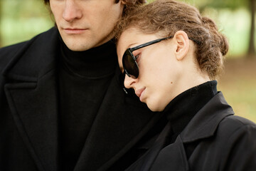 Wall Mural - Close up of young woman leaning hand on husbands shoulder while saying goodbye at outdoor funeral ceremony