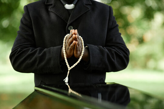 Close up of African American priest wearing black at outdoor funeral ceremony with focus on hands in prayer