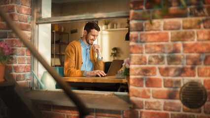 Leinwandbilder - Handsome Creative Male Entrepreneur Working Remotely on Laptop Computer from Home. Freelance Businessman Using Portable Device, Developing e-Business Project. Into Window From Outdoors View.