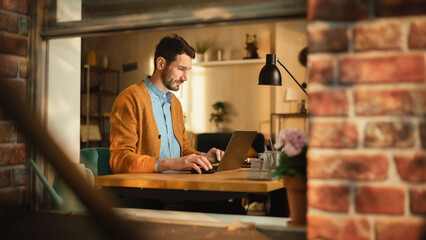 Aufkleber - Handsome Man Typing on Laptop Computer in Loft Apartment, Sunny Day Outside. Creative Male Checking Social Media, Browsing Internet. Freelancer Working From Home. View From Outdoors into Window.