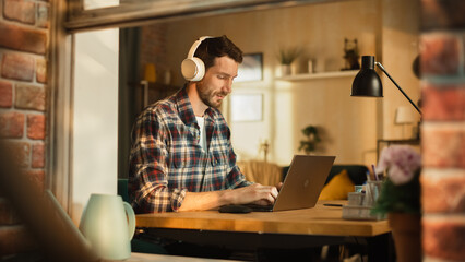Leinwandbilder - Modern Freelancer Wearing Headphones and Typing on Laptop, Creating Content for Social Media. Entrepreneur Working Remotely at Home Office, Managing e-Business. View From Outdoors into Window.