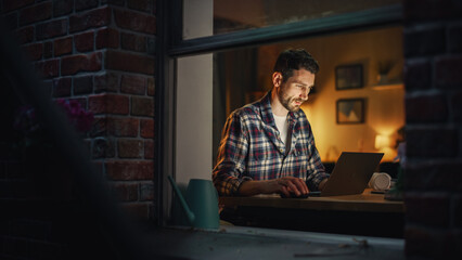 Aufkleber - Focused Man Working on Laptop Late in the Evening Finishing Important Project at Home Office. Freelancer Working Remotely. Warm Lit Cozy Apartment. View From Outdoors into Window.