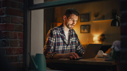 Aufkleber - Serious Man Working on Laptop Late in the Evening Finishing Important Project at Home Office. Freelancer Working Remotely. Warm Lit Cozy Apartment. View From Outdoors into Window.
