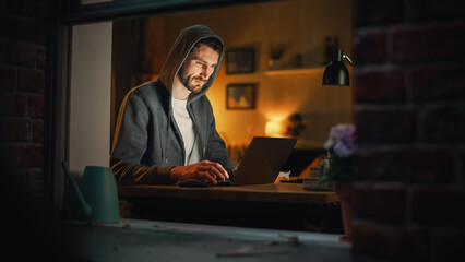 Aufkleber - Professional Male Programmer Writing Code for Complex Project and Working Remotely on Laptop From Home Office. Freelance Software Engineer Designs App in Apartment. View From Outdoors into Window.