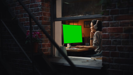 Aufkleber - Female Designer Using Desktop Computer with Green Screen Chroma Key Monitor. Remotly Working Manager Listening to Music or Podcast in Headphones, Freelancer Working at Night. Inside the Window Shot.