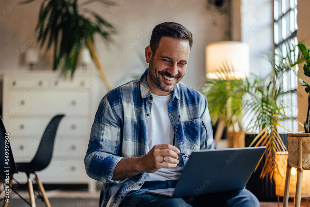 Happy man using a laptop, being at the office, holding his glasses ...