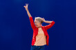 © VISTA by Westend61 - Happy mature woman gesturing peace sign and dancing in front of blue wall