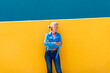 © VISTA by Westend61 - Mature woman with arms crossed leaning on colored wall