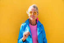 Smiling Mature Woman Wearing Sunglasses In Front Of Yellow Wall