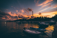Wide-angle Low-key View Of A Jetty On A Tropical tourist Island With An Atmospheric Sunset In The Background; An Ocean Pier With A Few Speedboats And Ferry Vessels With A Dramatic Evening Cloudscape