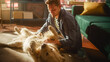 © Gorodenkoff - Successful Young Adult Man Playing with His Dog at Home, Active Golden Retriever. Man Sitting on a Floor Teasing, Petting and Scratching an Excited Dog, Having Fun in the Loft Living Room Space.