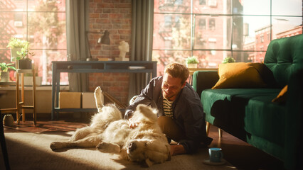 Young Adult Man Having Fun and Playing with His Golden Retriever Pet on a Living Room Floor. Attractive Dog Owner Petting, Scratching and Teasing His Canine Best Friend at Home.