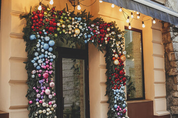 Wall Mural - Stylish christmas fir branches with many colorful baubles on building exterior. Modern christmas decor in city street. Winter holidays in Europe. Merry Christmas