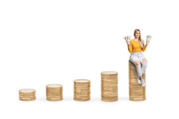 Canvas Print - Young female sitting on the highest pile of coins and holding banknotes