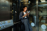 Fototapeta  - Young asian woman using smart phone while standing in elevator