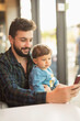 © Antonio Recena - Bearded man with baby son in bar near to window looking telephone