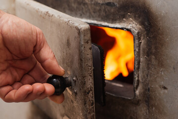 Hand of a man closing the door of solid fuel boiler. House heating, warmth at home in cold winter period