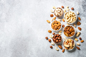 Wall Mural - Assortment of nuts in bowls. Cashew, hazelnuts, pecan, almonds, brazilian nuts and pistachios at light table. Top view with copy space.