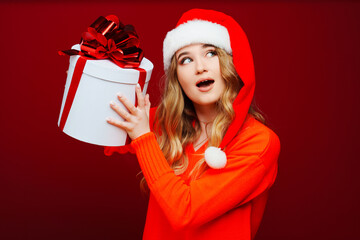 a beautiful young woman in a Santa Claus hat with a gift on a red background. 