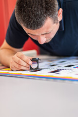 Wall Mural - Young man in the process of printing used color scales and loupe and management color correction. Spectrophotometer, print measuring.