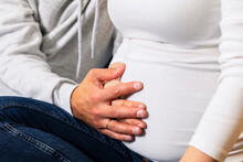 Closeup Of Couple, White Caucasian Man Touches, Holds Hand On Big Belly Of Pregnant Woman, Feeling Baby Movement. Happy Parenthood, Child Expectation. Adults Sit On Sofa. Magic Moments,baby Horizontal