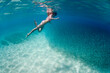 © Cavan Images - A girl swimming underwater with large school of fish in Hawaii.