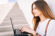 © Cavan Images - Front view of a happy student girl working with a laptop in the stairs of an university
