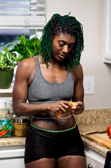 Wall Mural - Black woman with green dreadlocks cleaning and eating fruit in her kitchen