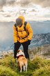 © Alberto - Mountaineer man in yellow coat, backpack and woolen cap summiting a mountain with his dog. Man climbing a mountain. Sport and adventure in nature