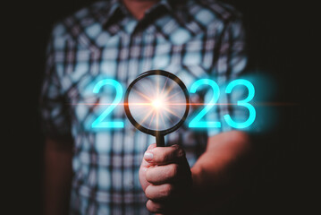Aufkleber - Male hand holding a magnifying glass With the number of the year 2023, it represents the search for new things in a new way
