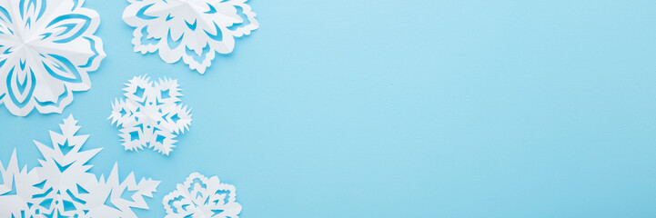 Wall Mural - White snowflake shapes created from paper on light blue table background. Pastel color. Closeup. Top down view. Wide banner. Handmade decoration elements for winter festive. Empty place for text.