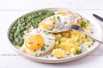 Wall Mural - Creamed spinach with fried eggs, sunny side up and boiled potatoes on a plate isolated on white background